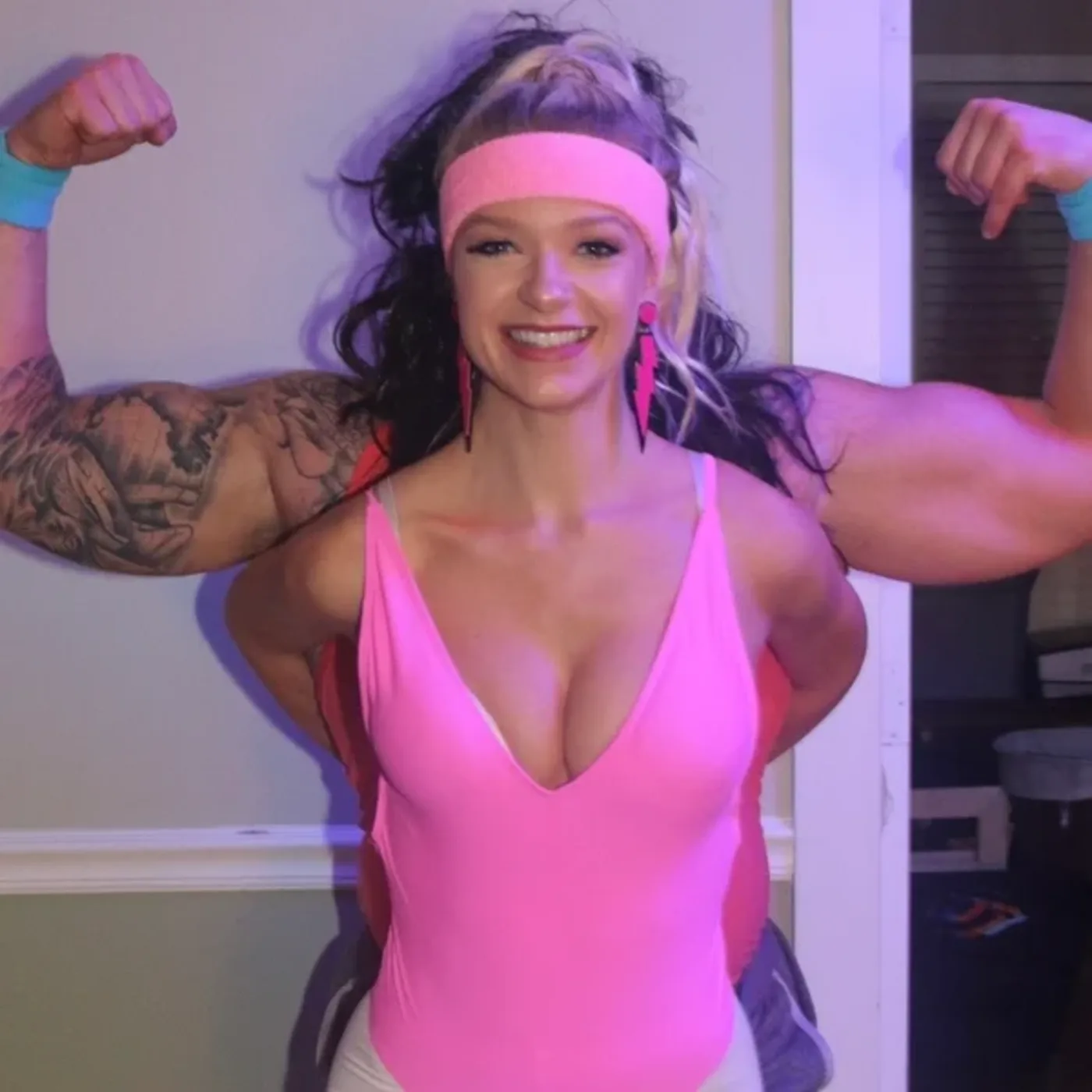 A guest in a pink tank and headband flexing in a mullet