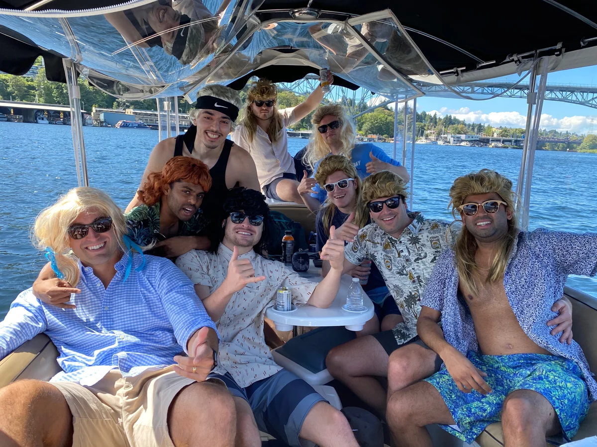 Group of friends on a boat at a lake party, all wearing mullet wigs