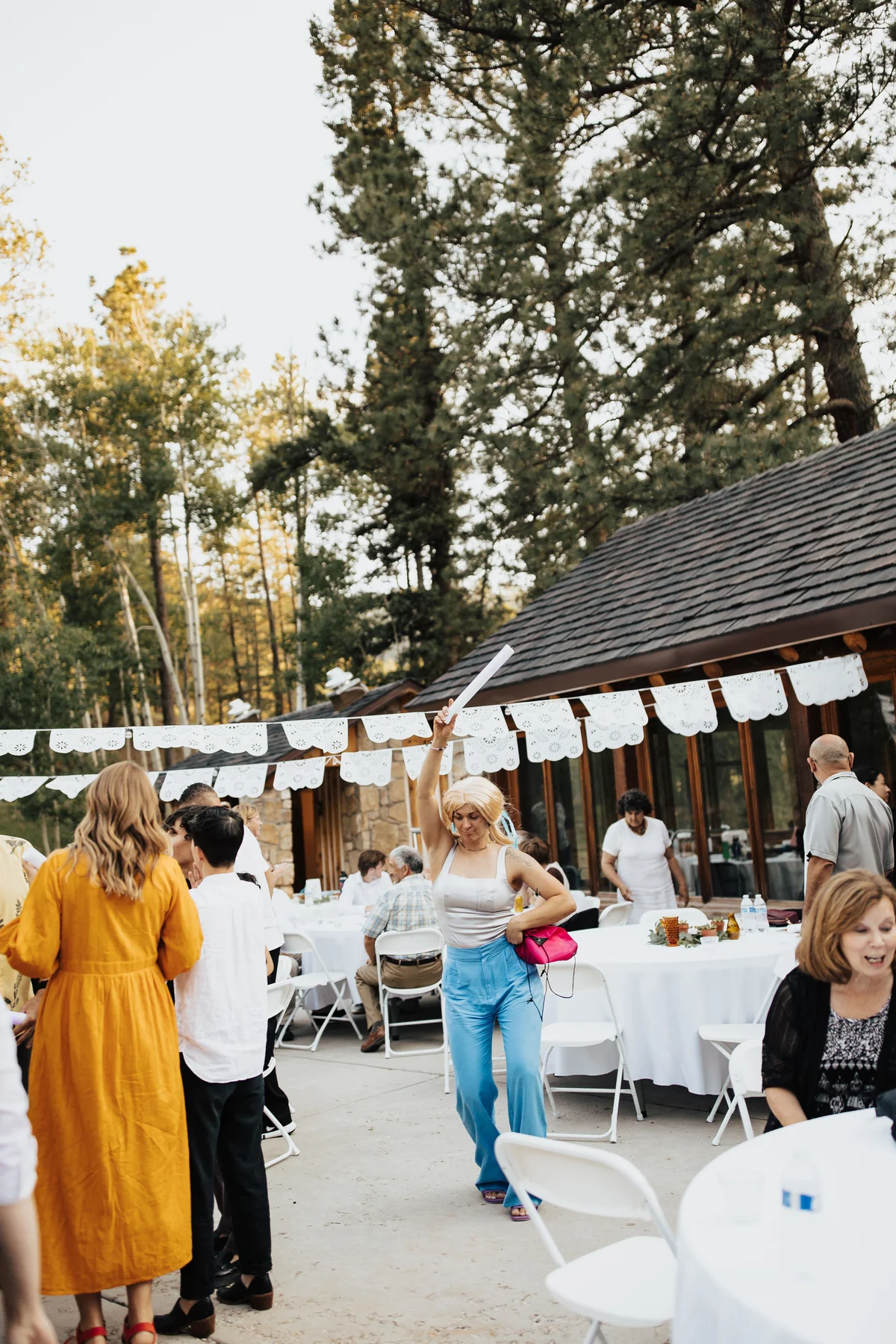 Wedding guest in a blonde mullet, arm raised mid-dance, reception in full swing.
