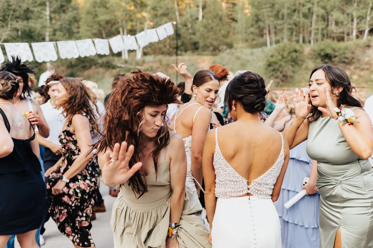 Bride in white on the dance floor, crowd in mullets around her.