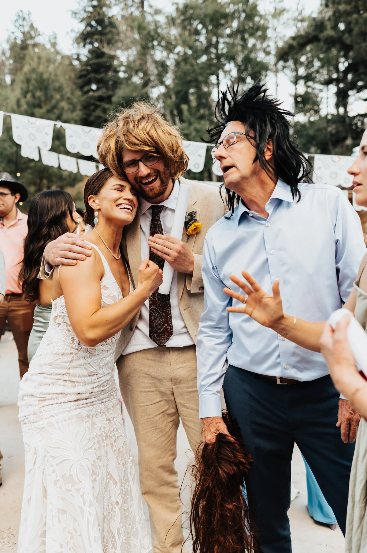 Bride leaning into groom in a blonde mullet, dad in a black mullet beside them.